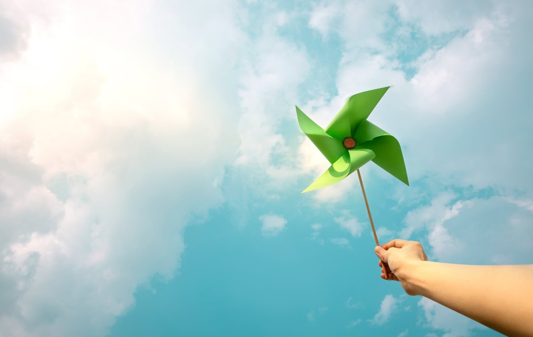 Hand holding a green pinwheel against blue sky, symbolizing renewable energy